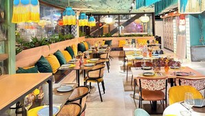Un restaurante con una decoración moderna, que cuenta con mesas y sillas de madera, una zona central con cojines e iluminación colgante.