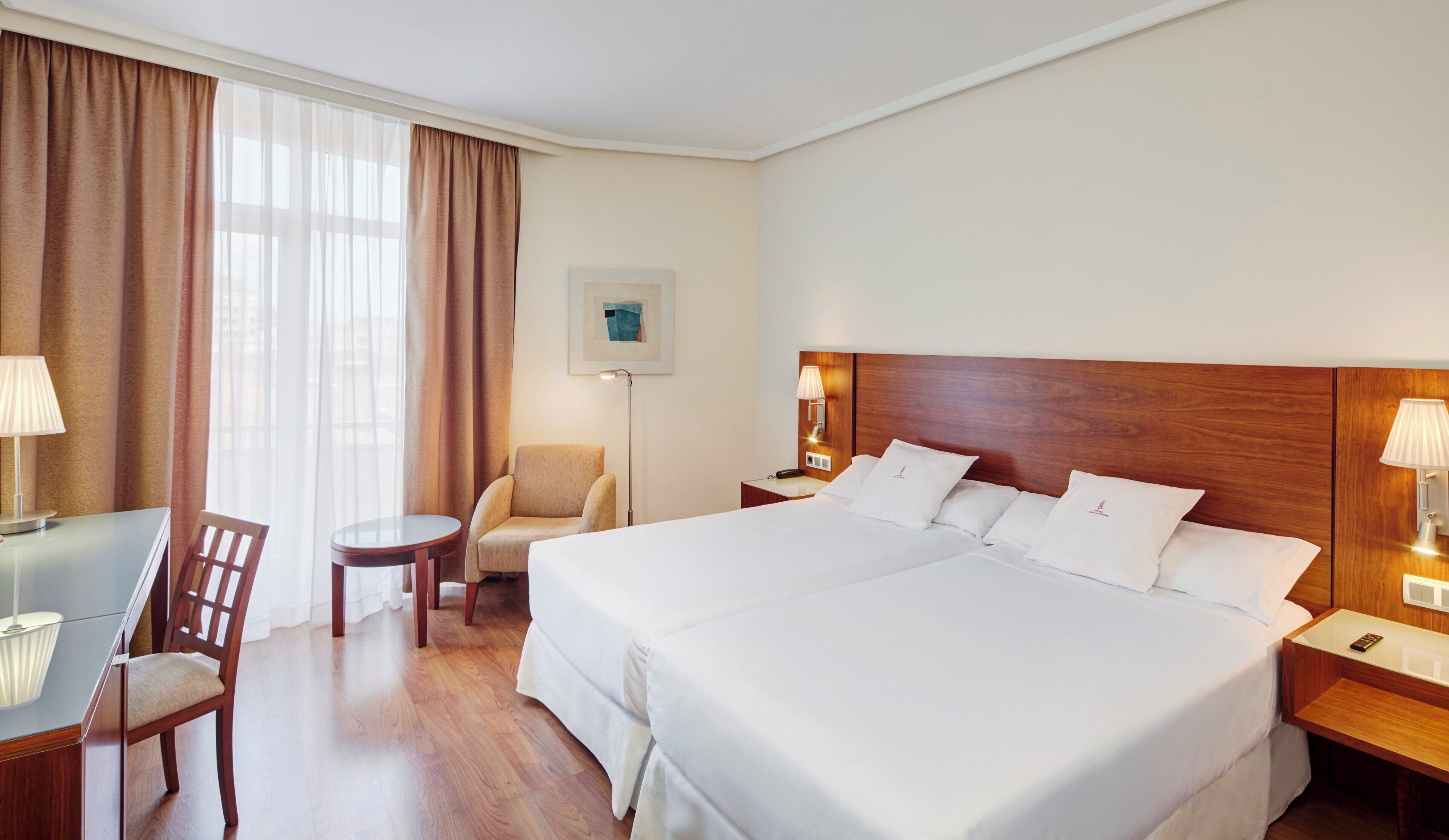 Een hotelkamer met twee bedden, een bureau met stoel, een klein tafeltje en een lamp.