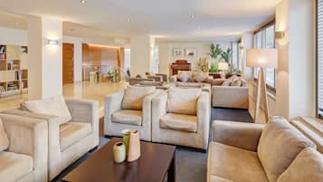 A spacious living area with multiple sofas and a coffee table, a bookshelf, and a piano in the background.