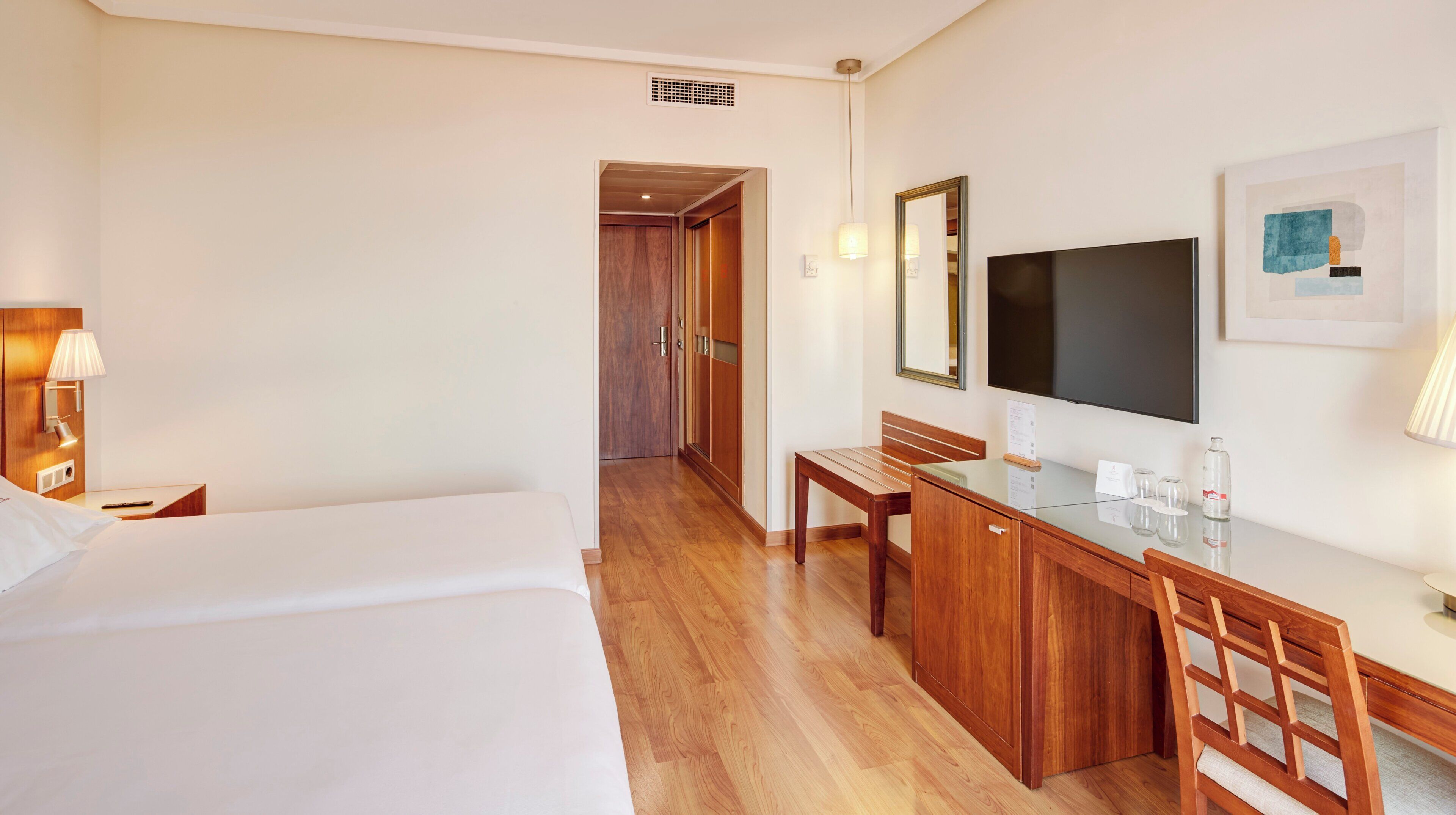 Una habitación de hotel con cama, escritorio, silla, televisor y espejo.