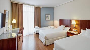 A hotel room with two beds, a desk, a chair, a TV, and a lamp.