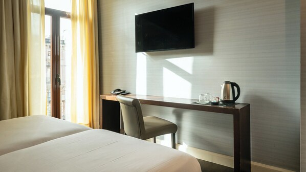 Una habitación de hotel con cama, escritorio con silla, televisor y cafetera.