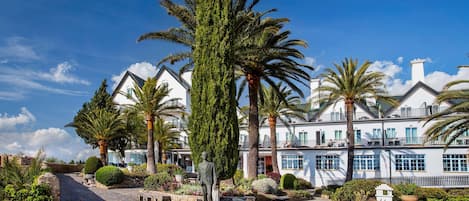 A coastal hotel with a paved walkway, palm trees, and a statue.