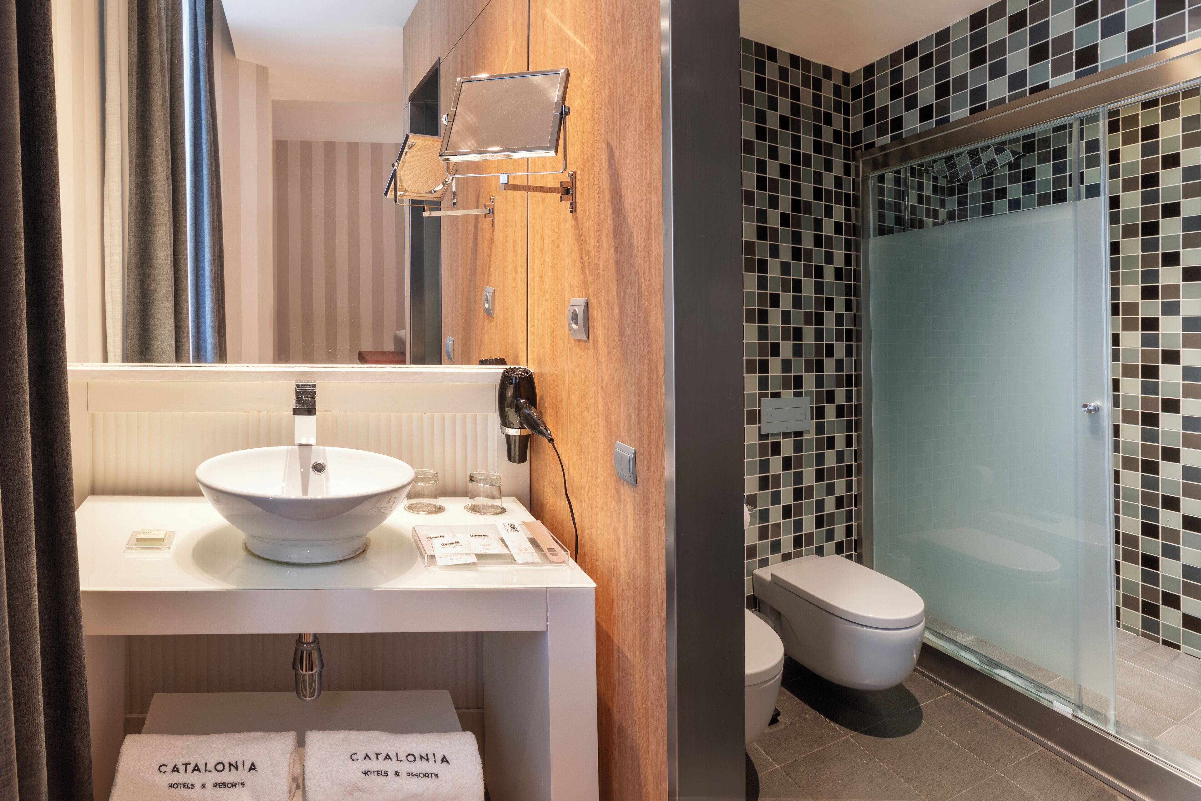A modern bathroom with a wooden vanity, a white sink, and a glass shower enclosure.