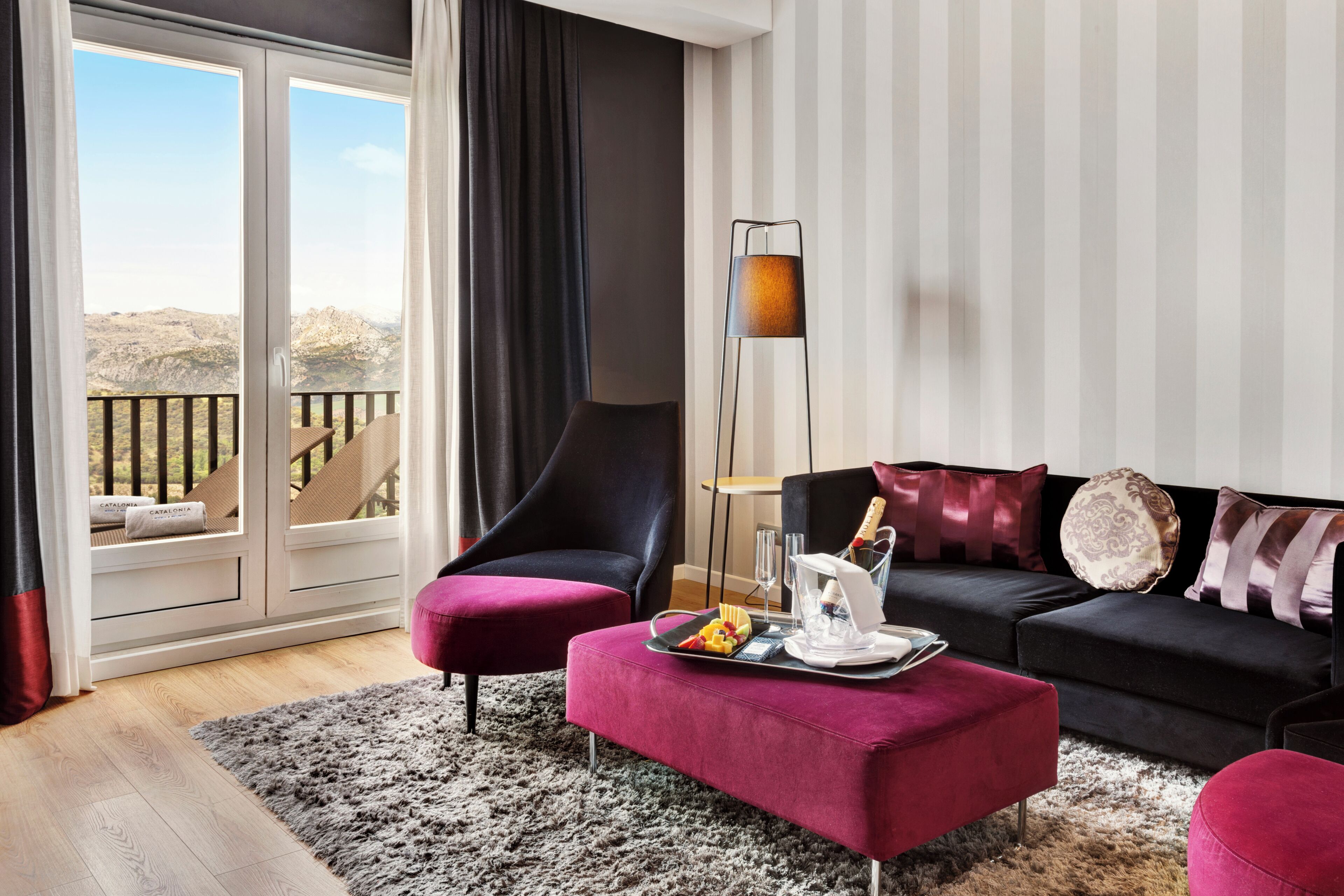 Un salon moderne avec un canapé noir, un pouf rouge et une lampe sur pied.