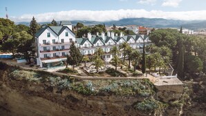 Un edificio grande de varios pisos con una fachada simétrica, un patio central con palmeras y vistas a montañas distantes.