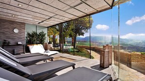 Zona de spa con sillones reclinables, camilla de masaje y vistas al paisaje a través de amplios ventanales.