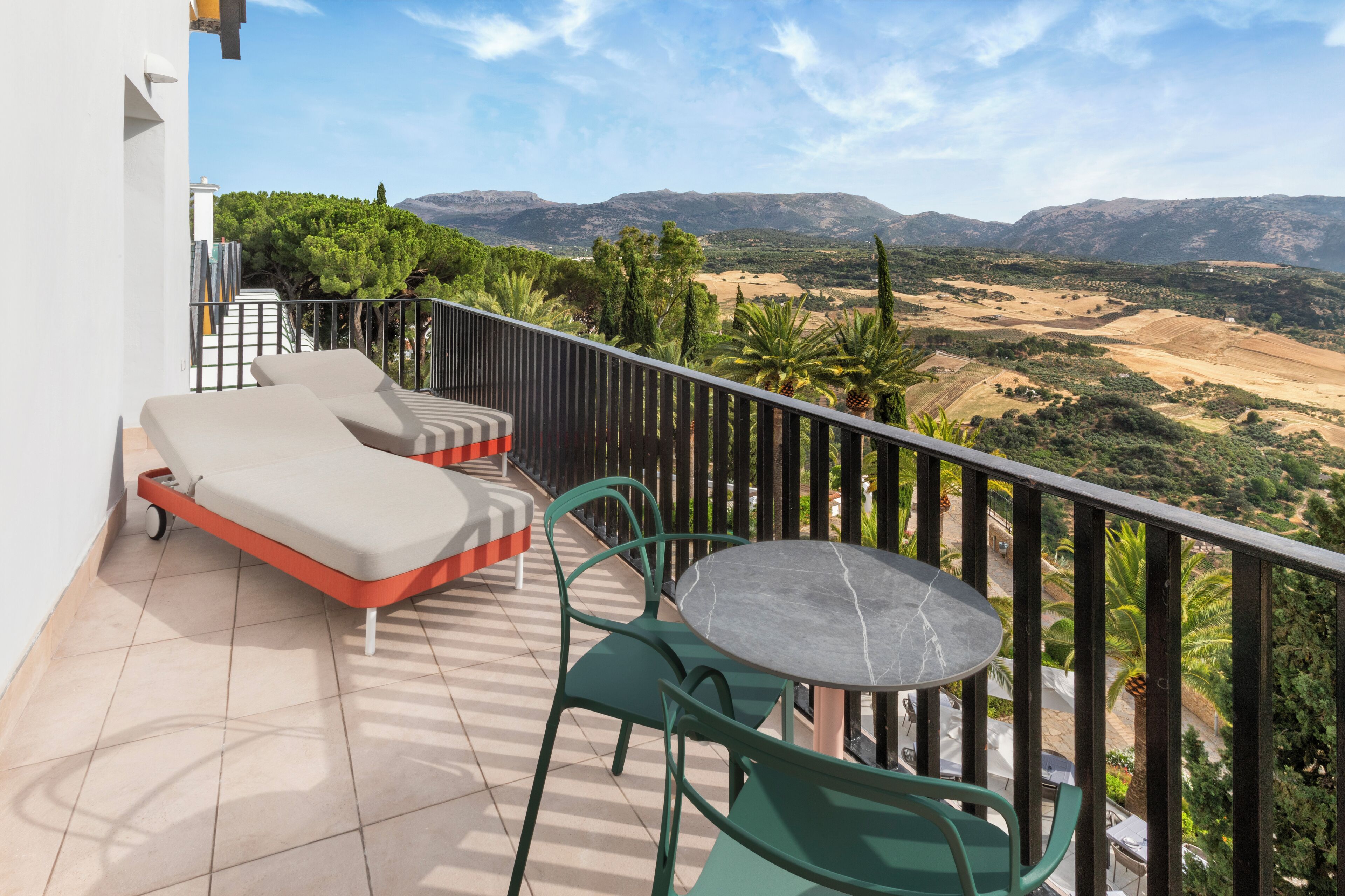 Un balcón con sofá, sillas y una mesa, con vistas a un paisaje montañoso.
