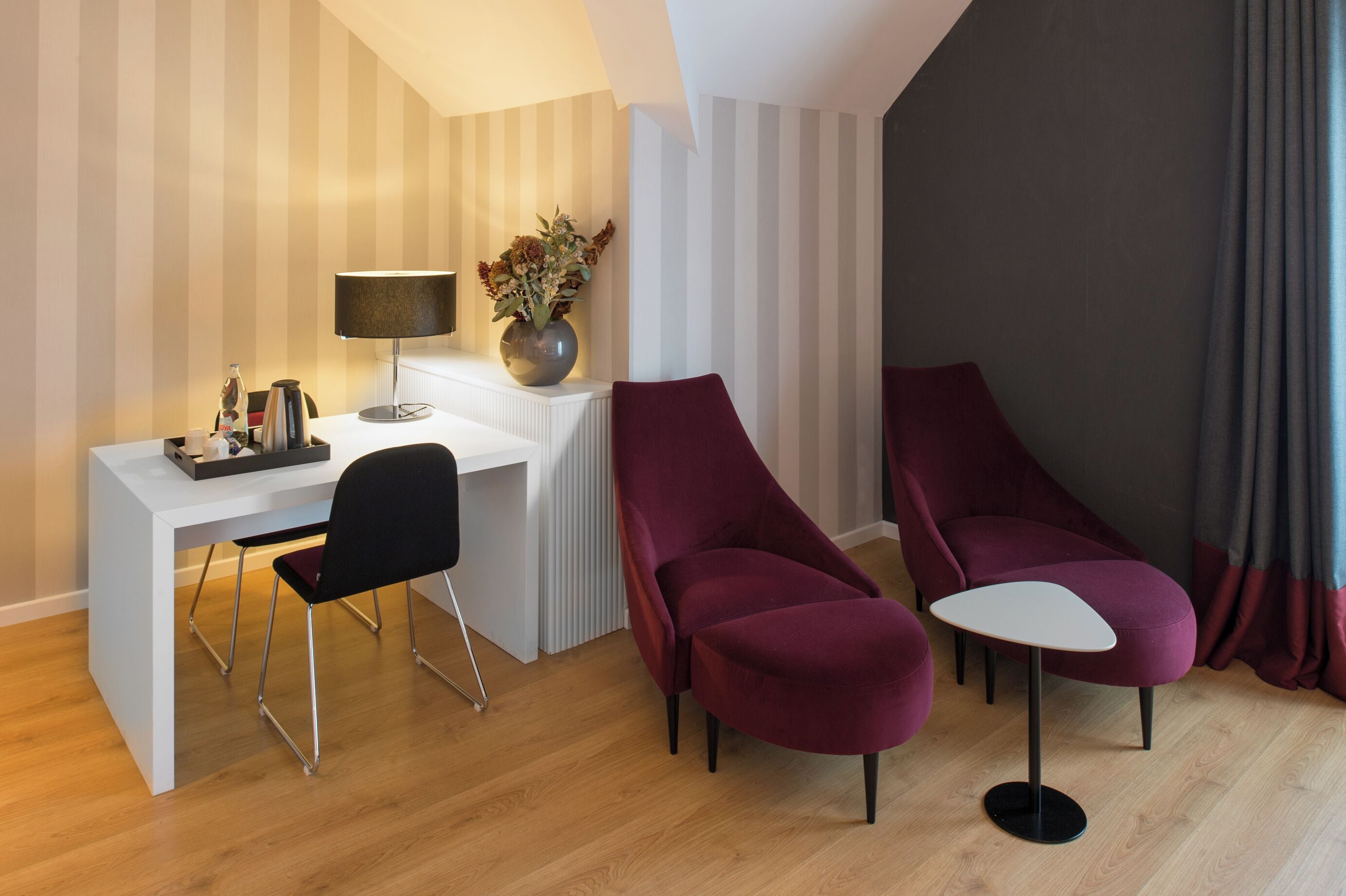 Ein modernes Zimmer mit einem weißen Schreibtisch, einem schwarzen Stuhl und zwei roten Sesseln.