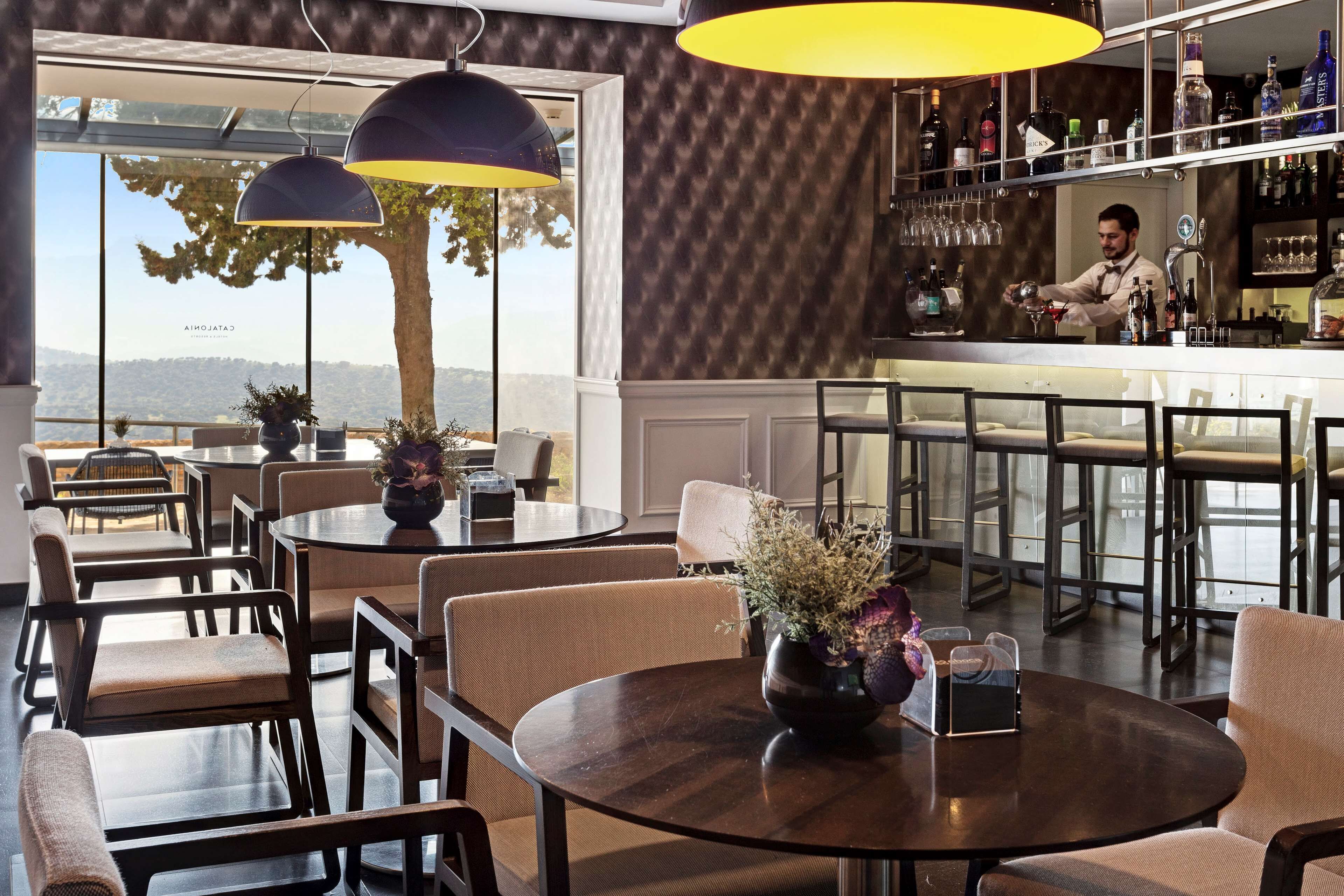 A bar area with a bartender, round tables with chairs, and a view of the outdoors.