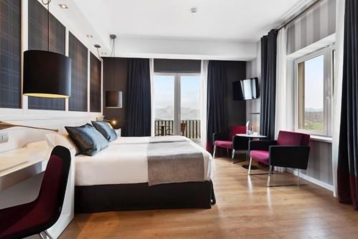 A hotel room with a bed, a desk, a chair, a TV, and a window with a view.