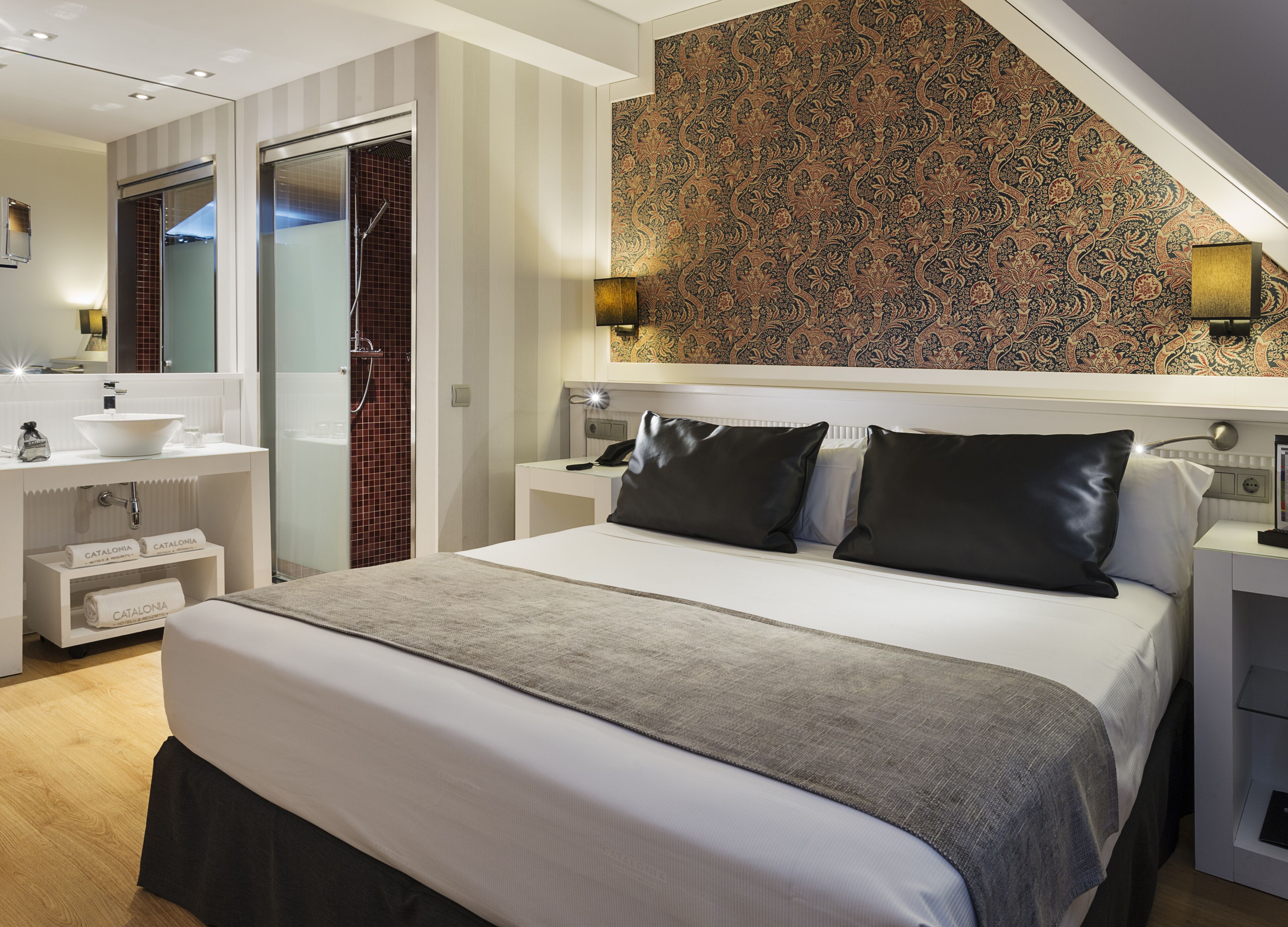 A modern hotel room with a large bed, a bathroom with a sink and mirror, and a patterned wall.