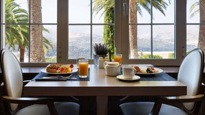 Una mesa de desayuno con croissants, fruta y zumo de naranja, con vistas a palmeras y montañas.