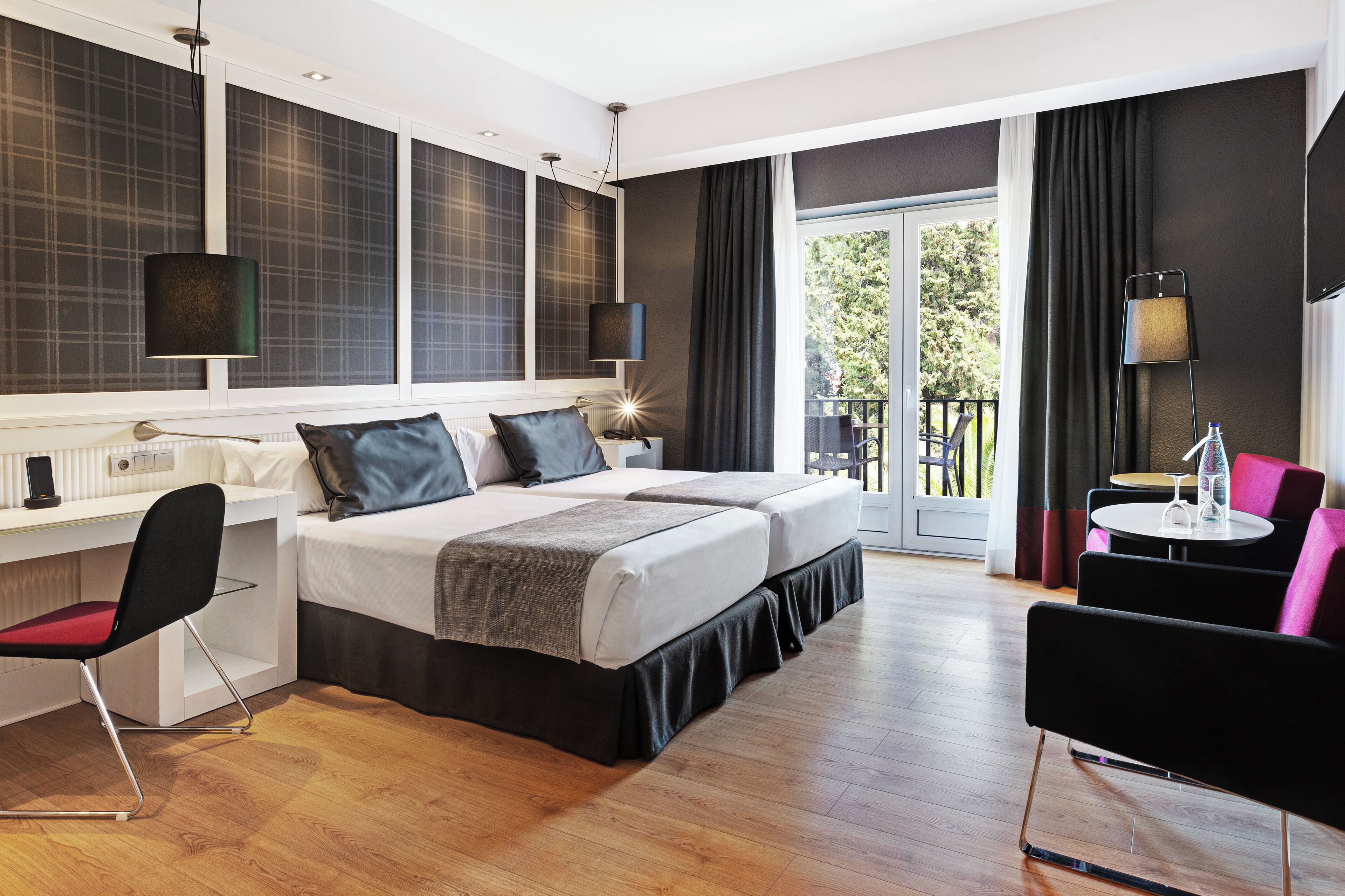 Een moderne hotelkamer met een groot bed, een bureau, een stoel en een balkon met een tafel en stoelen.