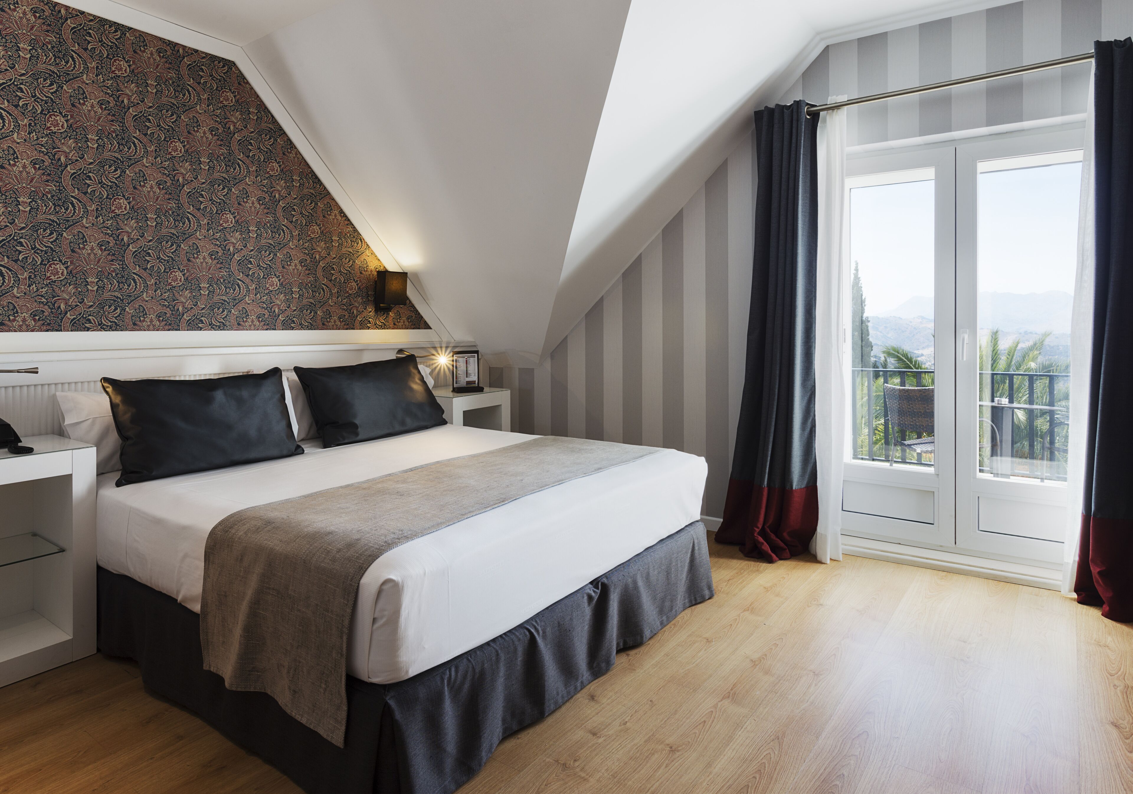 Camera moderna con un letto grande, un comodino, una lampada e vista all'aperto attraverso un'ampia finestra.
