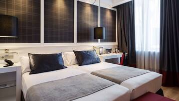 Habitació d'hotel amb dos llits, escriptori, telèfon i finestra gran amb cortines.