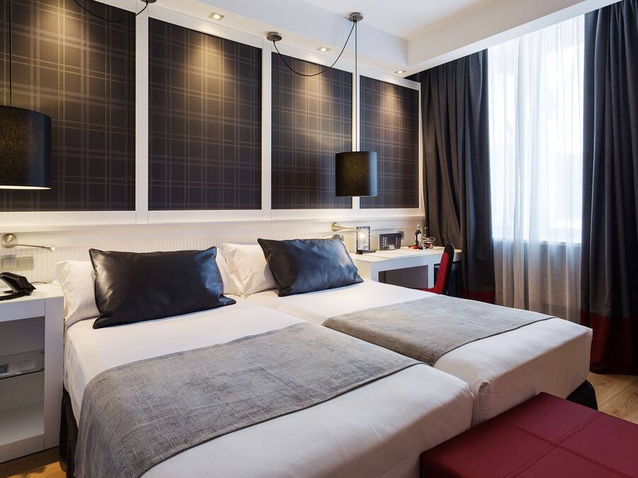 Habitació d'hotel amb dos llits, escriptori, telèfon i finestra gran amb cortines.
