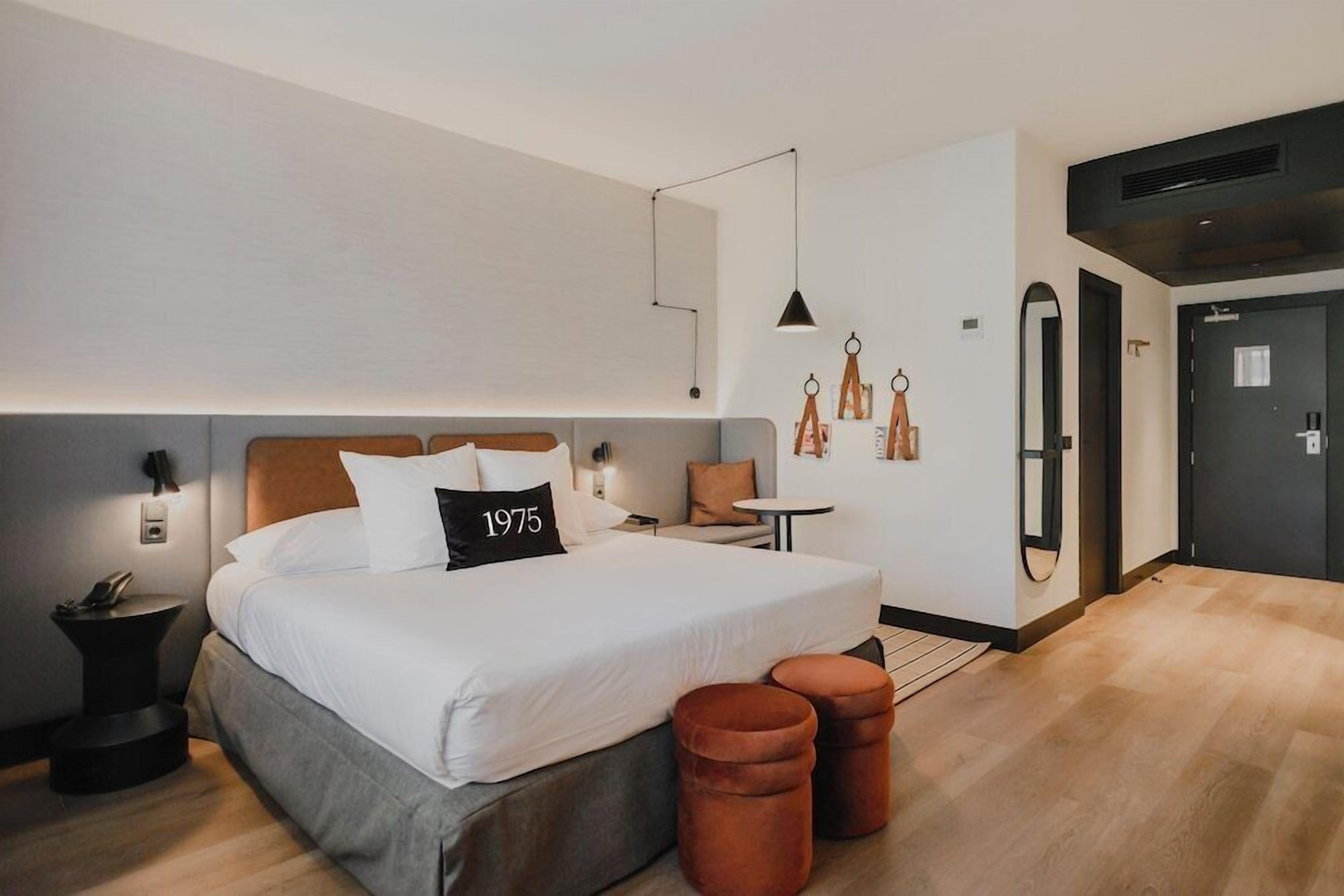 Quarto de hotel moderno com uma cama grande, uma mesa de cabeceira, uma pequena mesa redonda e um guarda-roupa.
