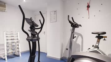 Un gimnasio con dos bicicletas estáticas, un soporte para mancuernas y un reloj de pared.