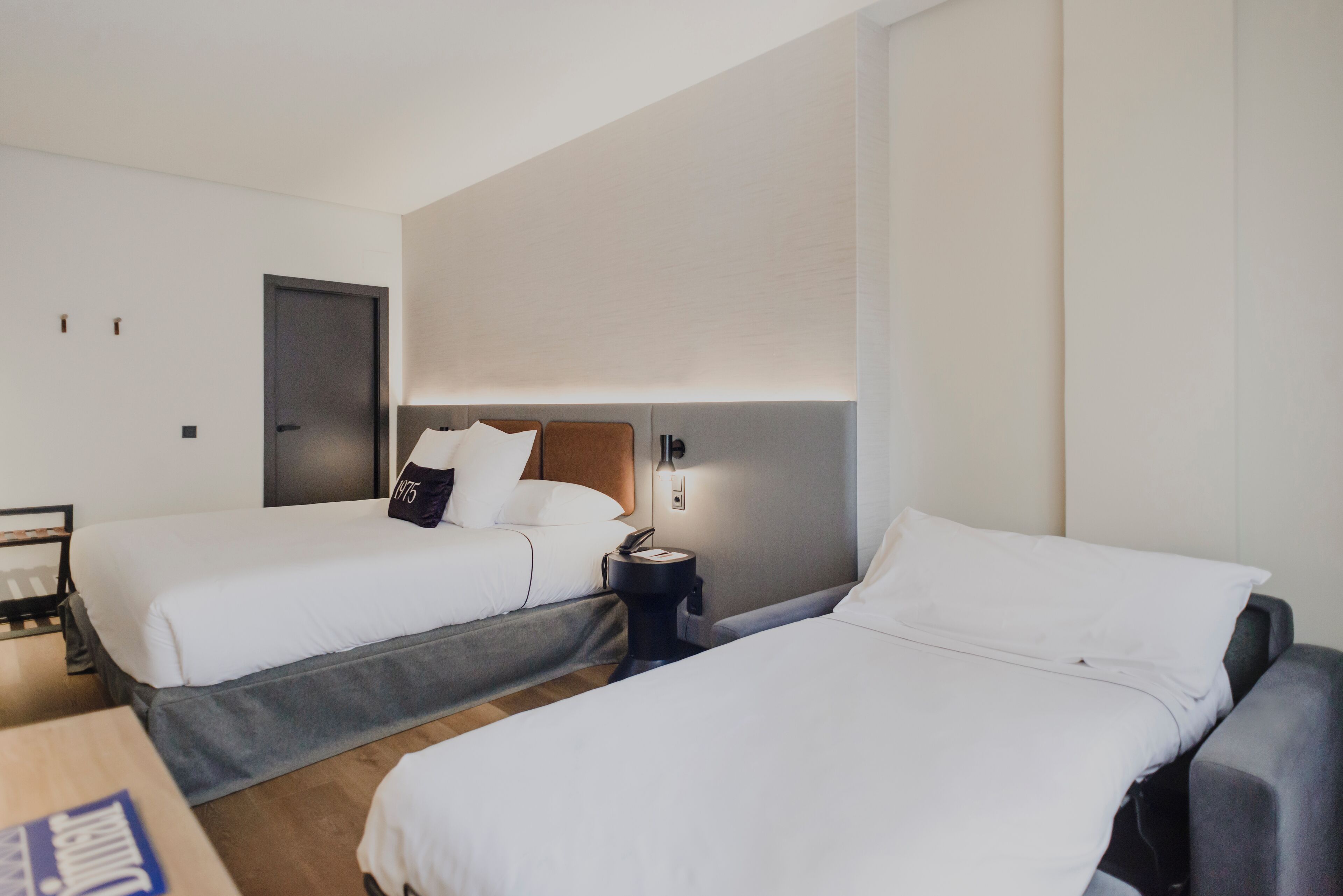 Une chambre d’hôtel avec deux lits simples, une table de chevet avec une lampe et une porte.