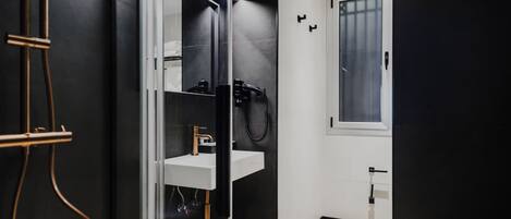 A modern bathroom with a glass shower enclosure, a white sink, and a blue stool.
