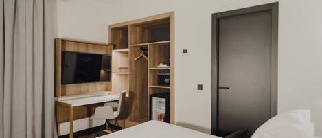 A hotel room with a bed, a desk with a chair, a TV, a wardrobe, and a door.