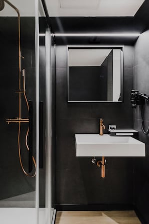 A modern bathroom with a glass shower enclosure, a white sink with copper fixtures, and a large mirror on the wall.
