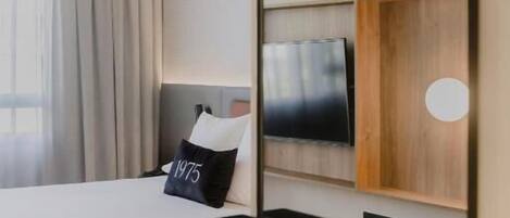 A modern hotel room with a bed, a desk, a chair, a TV, and a large mirror.