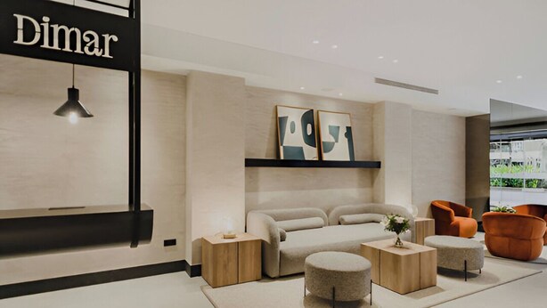 Un salon moderne avec un canapé, des poufs et des fauteuils orange. Un panneau noir portant le mot « Dimar » est accroché au mur.