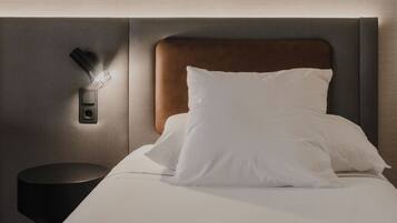 A neatly made bed with white linens and a wooden headboard, a small black nightstand with a lamp, and a textured wall.
