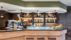 A bar area with a wooden counter, multiple stools, a variety of liquor bottles, and a display case with pastries. - Hotel Don Jaime 54 (Zaragoza)