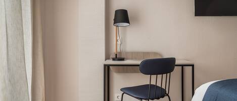 A hotel room with a desk, chair, and a bed.