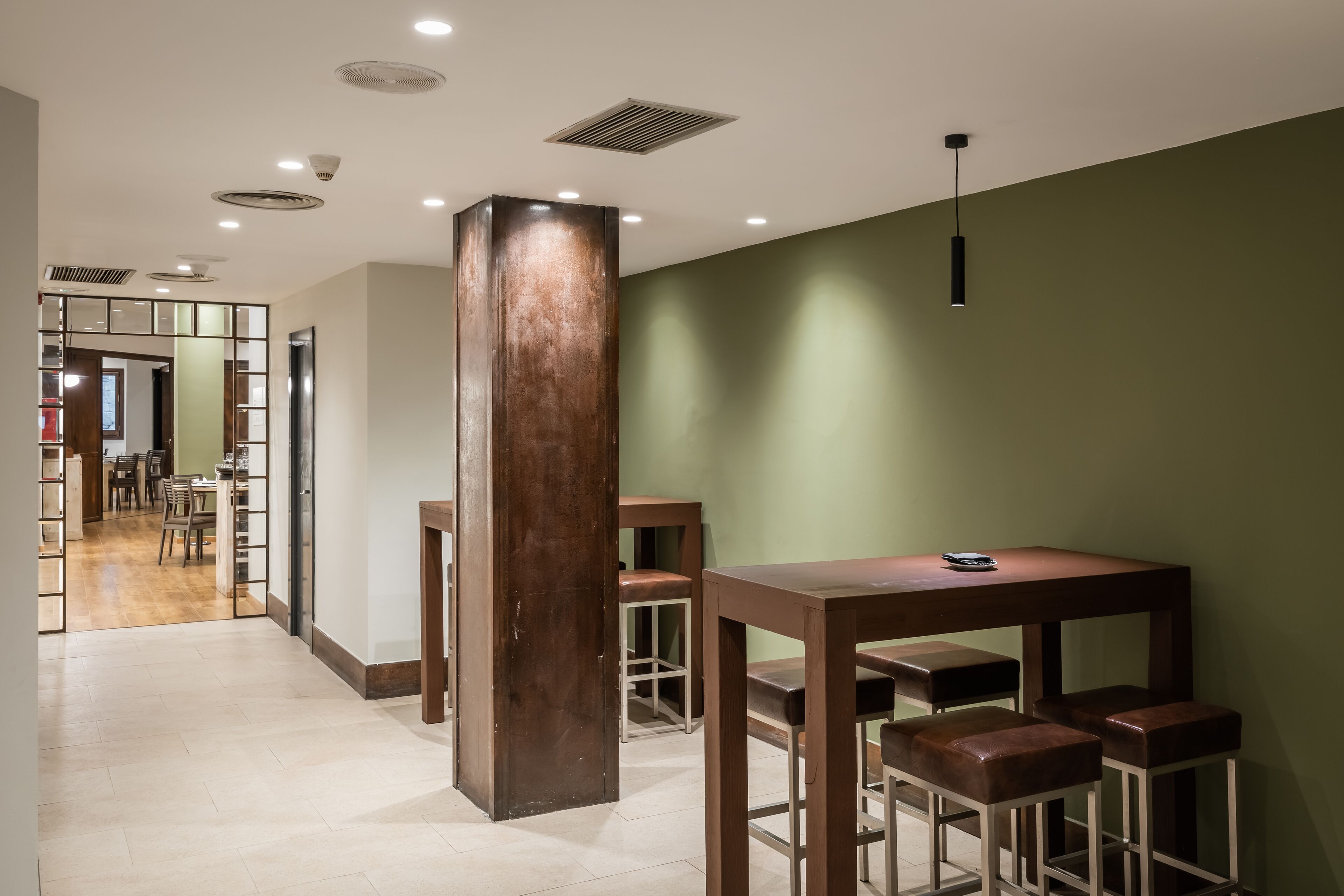 Un interior moderno con una mesa de madera y taburetes de bar, una pared de acento verde y vistas a un comedor.