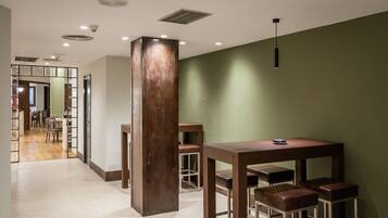 A modern interior with a wooden table and bar stools, a green accent wall, and a view into a dining area.