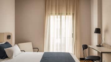 Una camera d'albergo con un letto, una scrivania, una sedia e una finestra con tende.