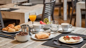 A breakfast setting with croissants, cereal, toast, fruit, and coffee on a wooden table. - Hotel Don Jaime 54 (Zaragoza)