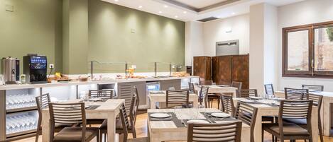 Un espace repas moderne comprenant plusieurs tables et chaises, un coin café et une cuisine.