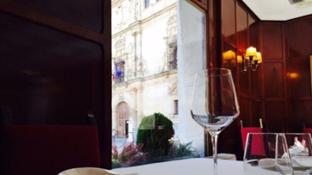Una mesa de comedor dispuesta con platos blancos, una copa de vino y cubiertos.