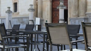 Mesa y sillas en terraza exterior, edificio de piedra con una puerta de madera grande y un letrero.