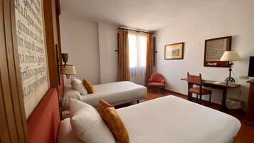 Habitación de hotel con dos camas, un escritorio, una silla, una lámpara y una ventana con cortinas.