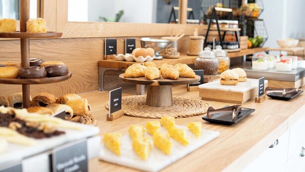 Un bufé de desayuno con diversas pastelerías y postres expuestos sobre pedestales y bandejas de madera.