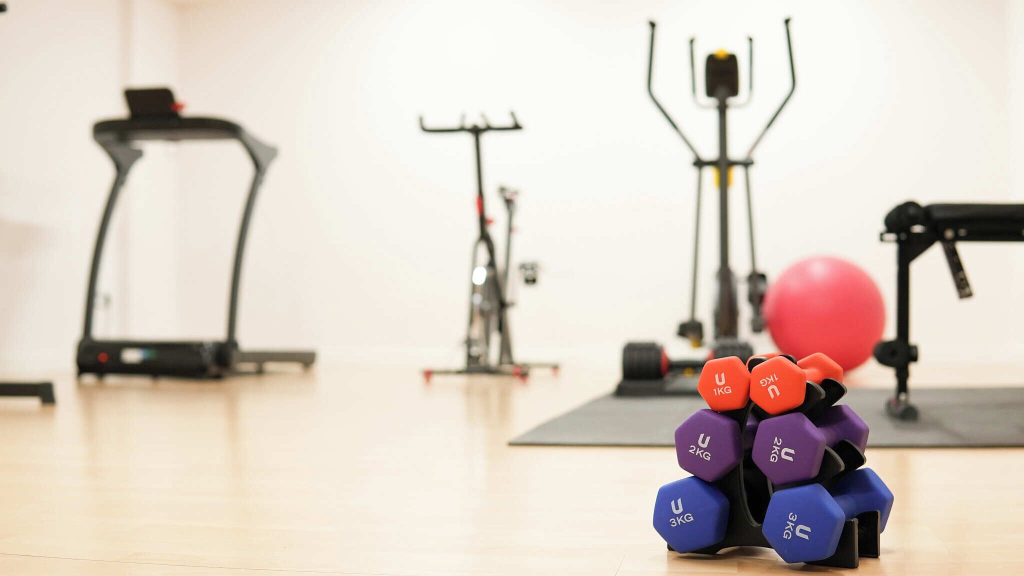 Un gimnasio con equipo de ejercicio, incluyendo cintas de correr, una bicicleta estática y mancuernas.