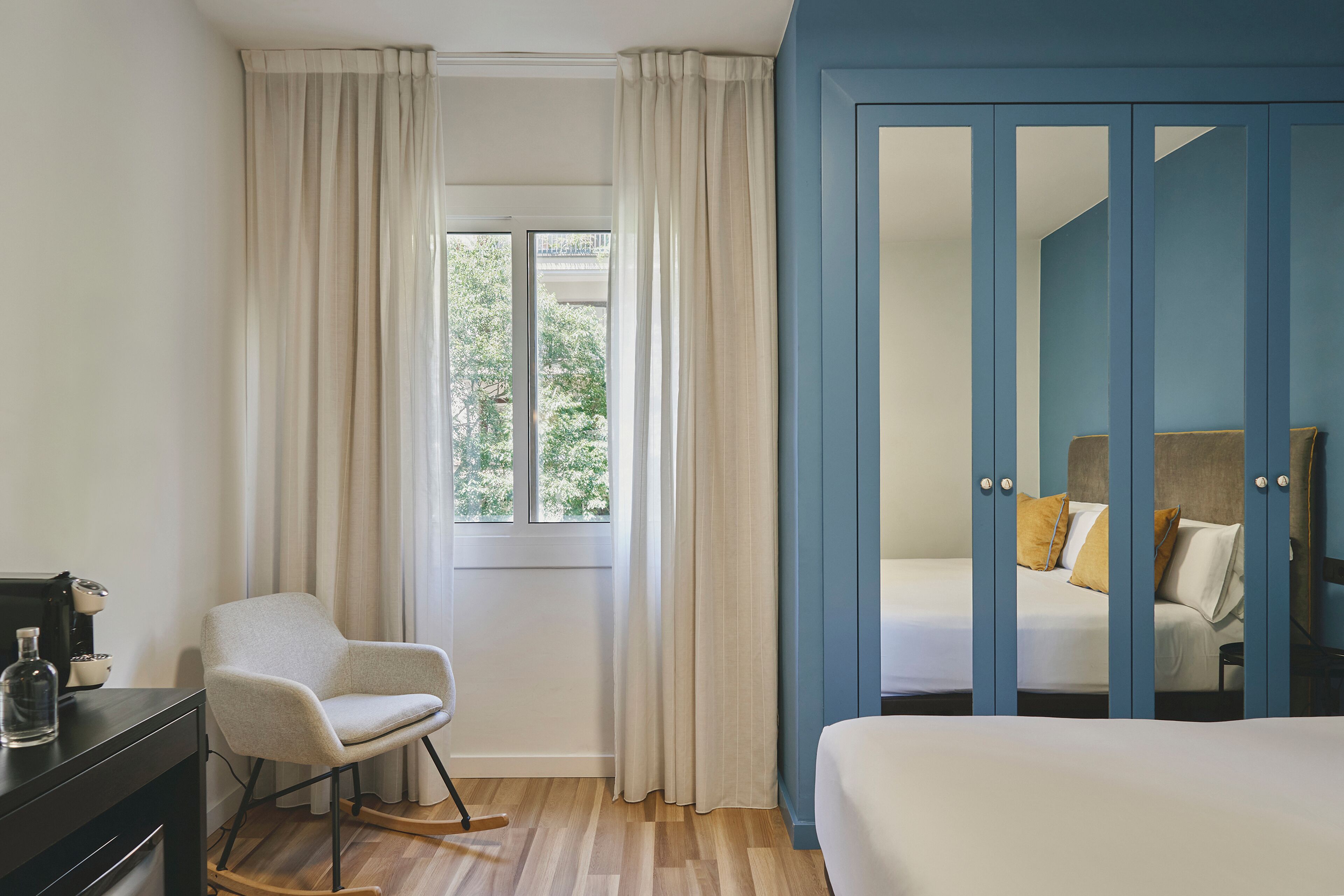 Ein Schlafzimmer mit Bett, Sessel, Schreibtisch und einem Fenster mit Vorhängen.