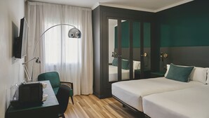 Una habitación de hotel con escritorio, silla, lámpara y cama con dos almohadas.