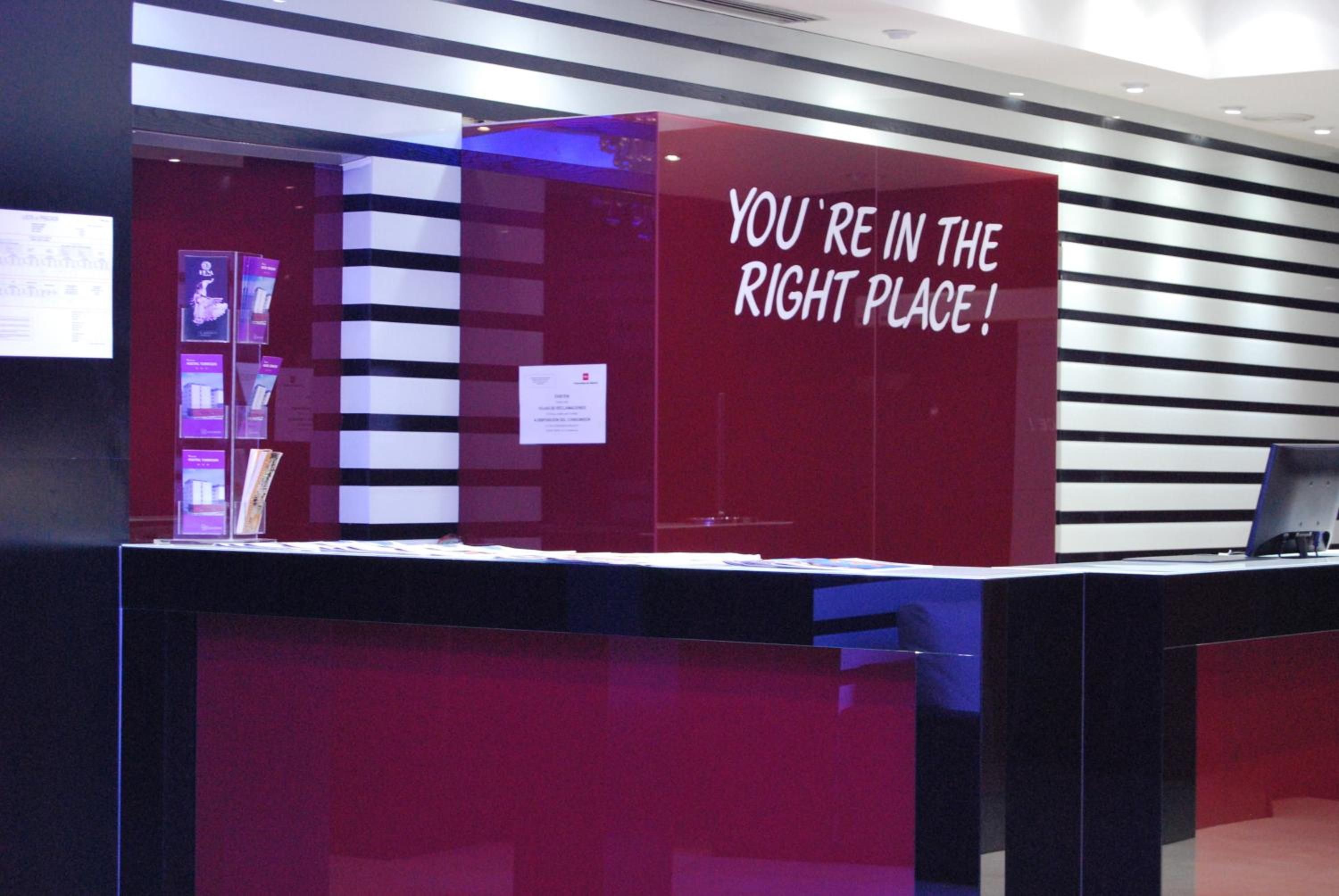 A reception desk with a red panel and a sign that reads 'YOU'RE IN THE RIGHT PLACE!'