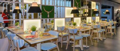 Un espace repas doté de plusieurs tables et chaises, éclairé par des suspensions, et présentant un design moderne avec des meubles en bois et des panneaux décoratifs.