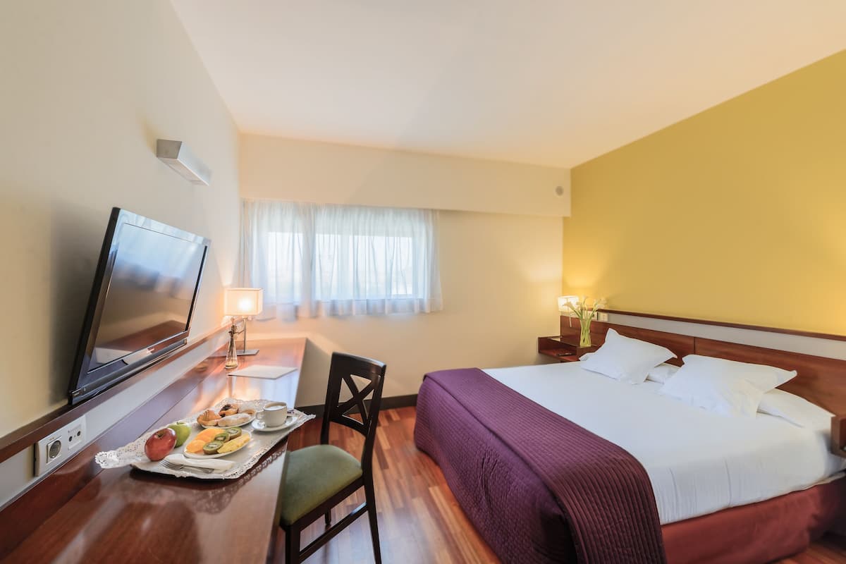 A hotel room with a bed, a TV, a desk with a lamp, and a breakfast tray.