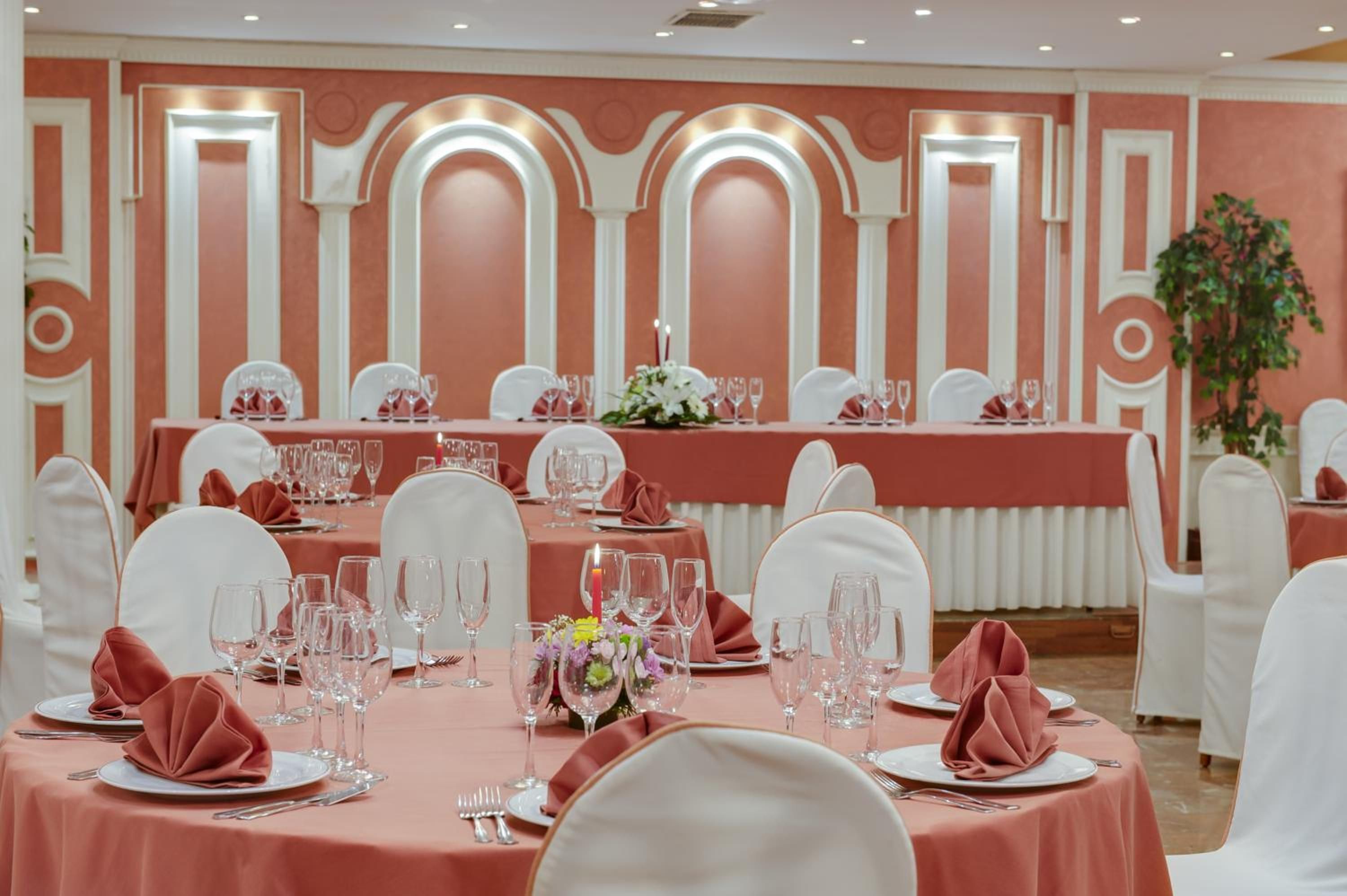 A banquet hall with round tables, white chairs, and red tablecloths.