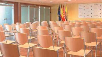 Una sala de conferències amb files de cadires, una pissarra amb logotips i banderes a la paret.