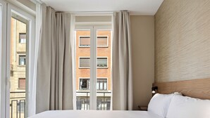 A hotel room with a large bed, a view of a brick building, and a window with curtains. - Hotel Avenida (Pamplona)